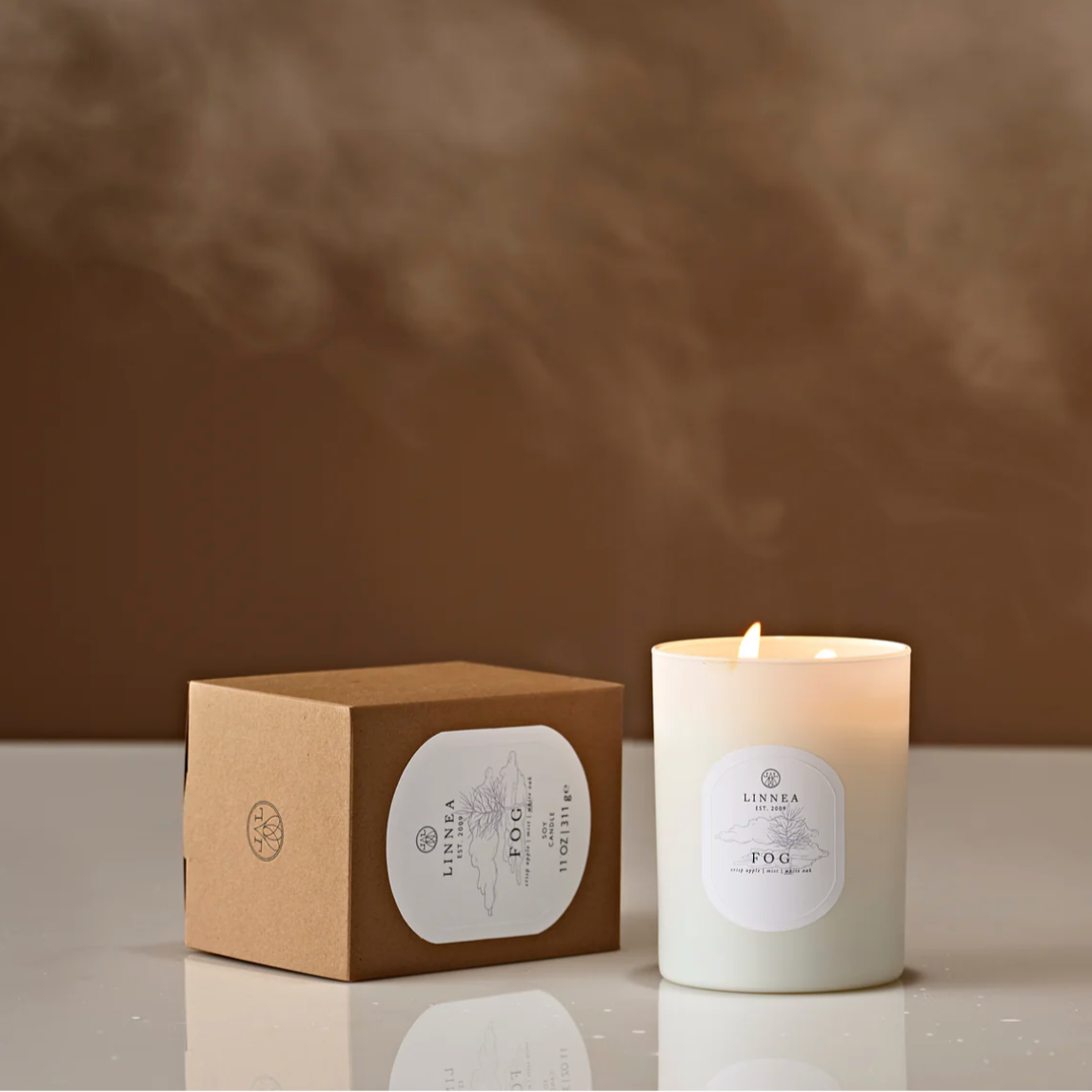 Candle and its packaging on a reflective surface with a brown background