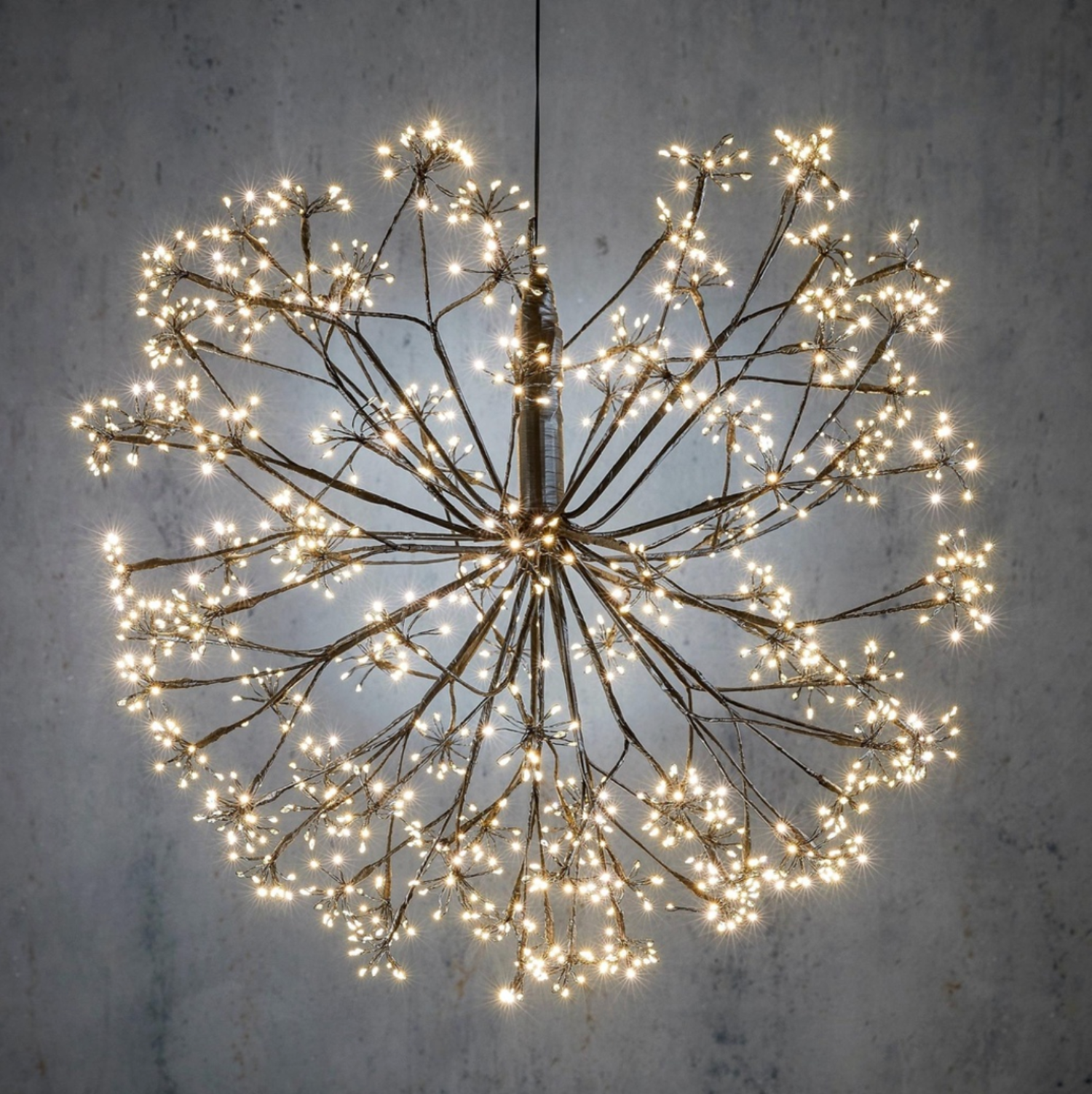 Decorative light fixture with branches and small lights against a gray wall