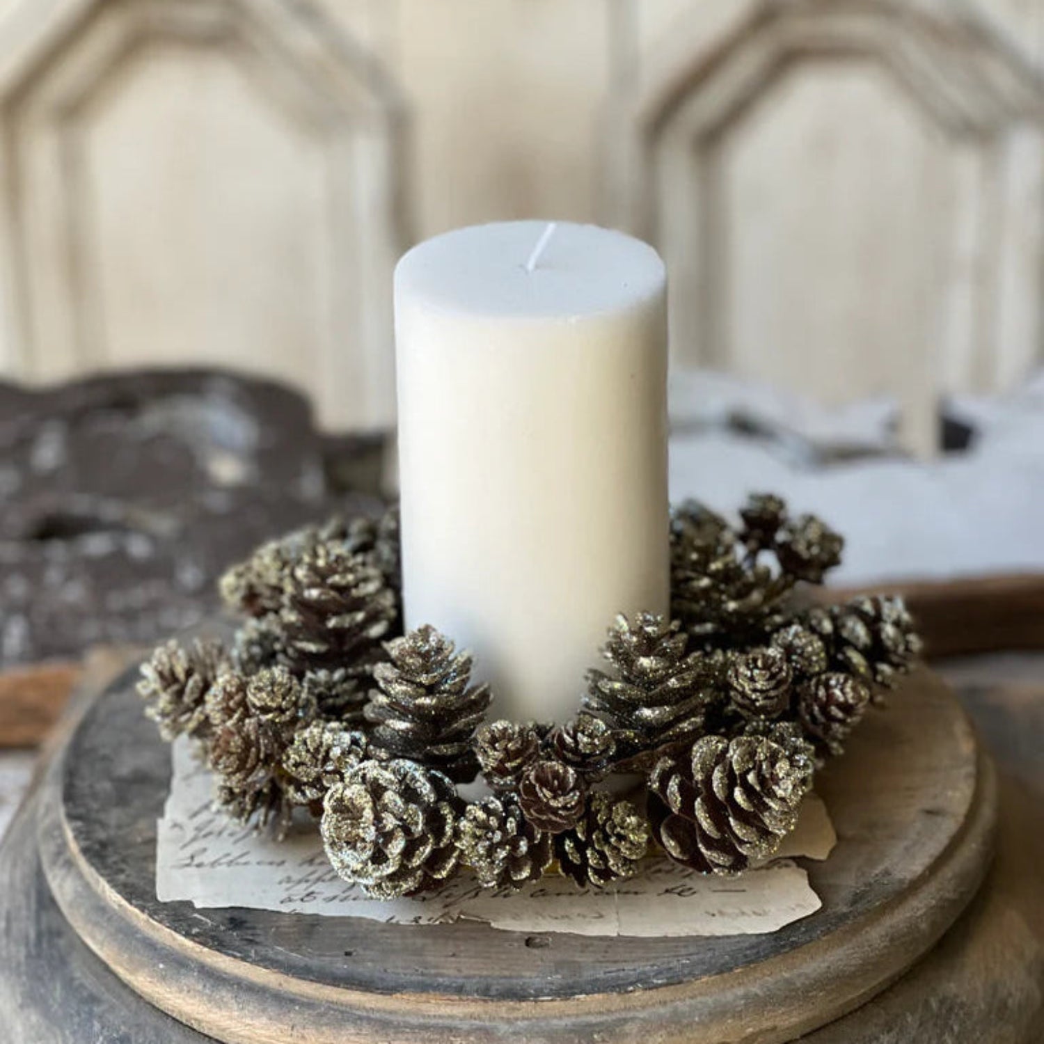 White candle in a decorative holder made of pinecones on a wooden surface.