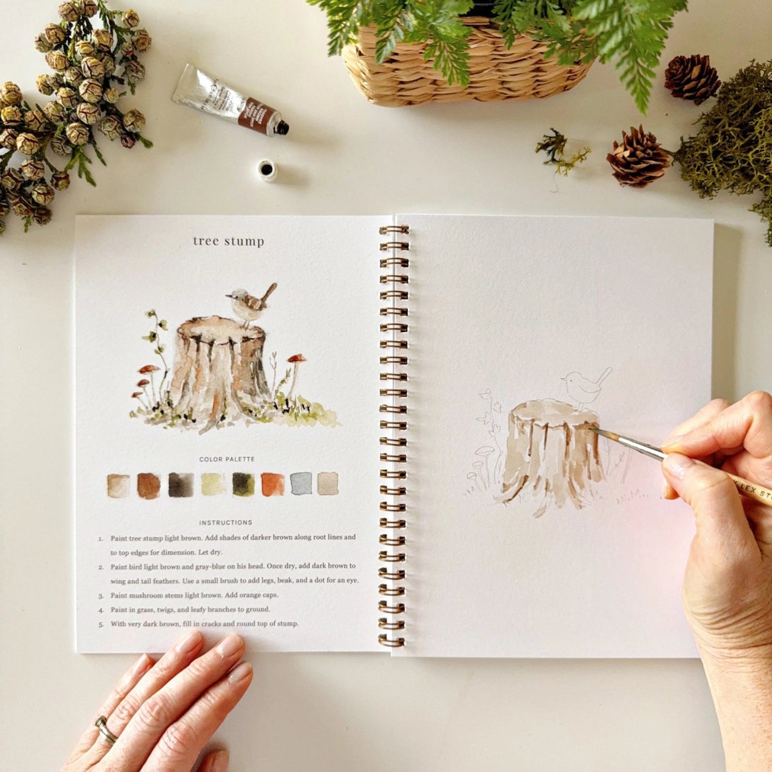 Person drawing a tree stump illustration from a coloring book with a paintbrush.