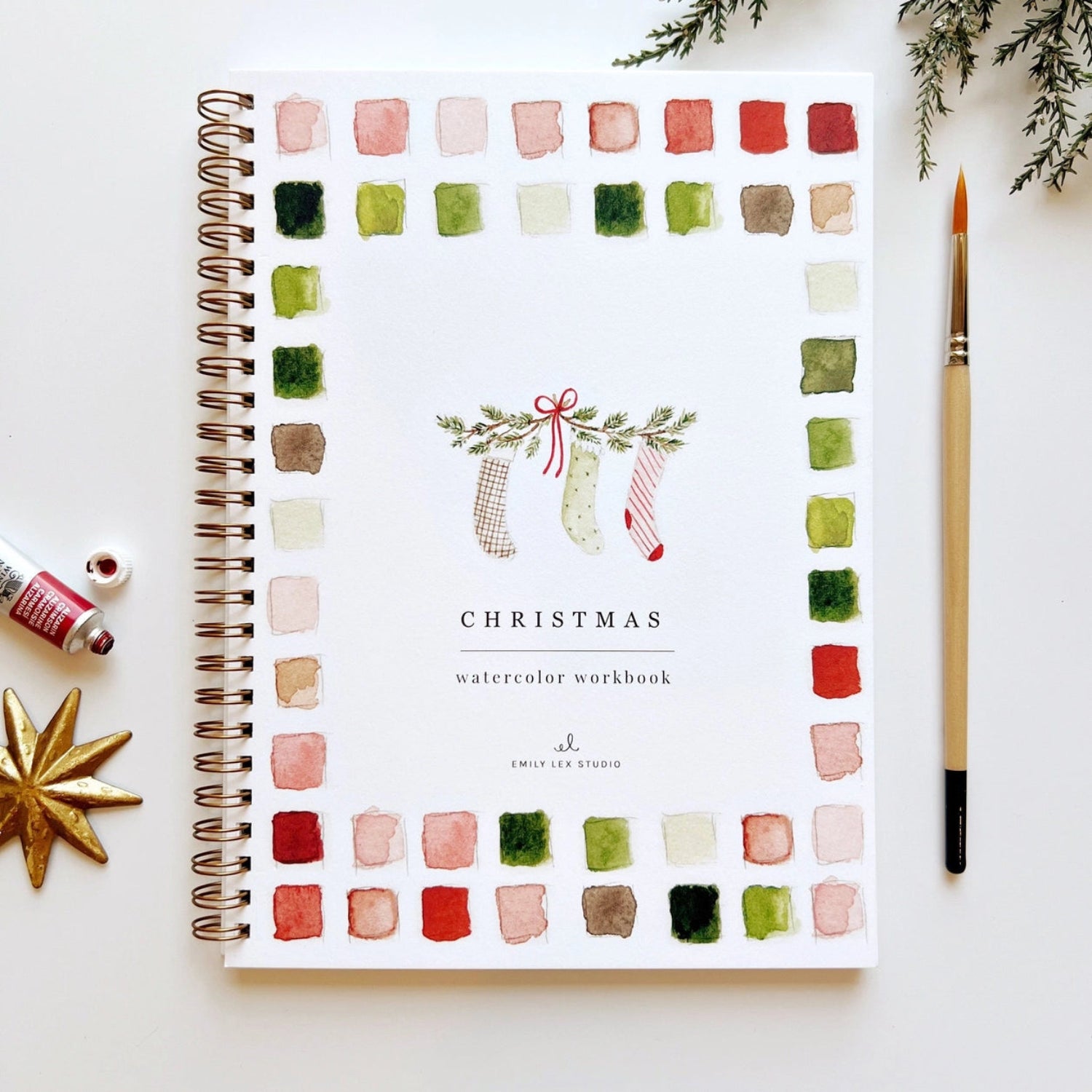 Christmas watercolor workbook with color swatches on a white surface with decorative items.