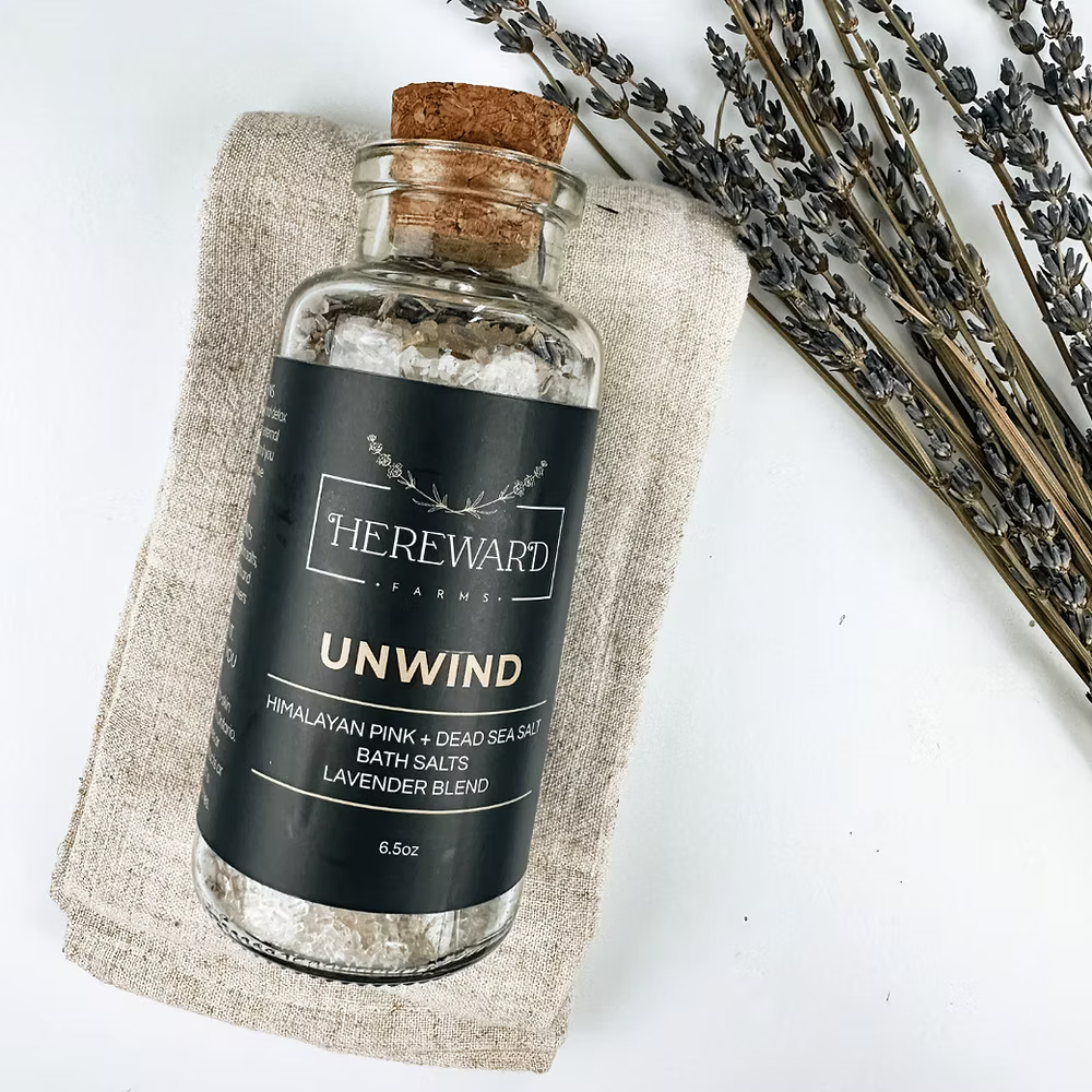 Bottle of 'Unwind' bath salts from Hereward Farms on a white background with lavender.