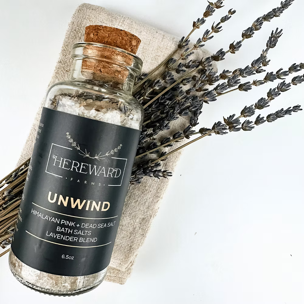 Bottle of 'Unwind' bath salts from Hereward Farms with lavender on a white background