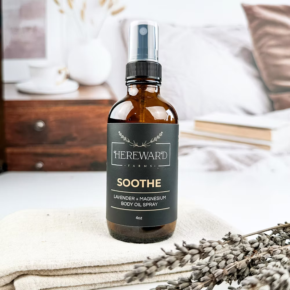 Hereward Farms Soothe lavender and magnesium body oil spray bottle on a textured surface with lavender flowers.