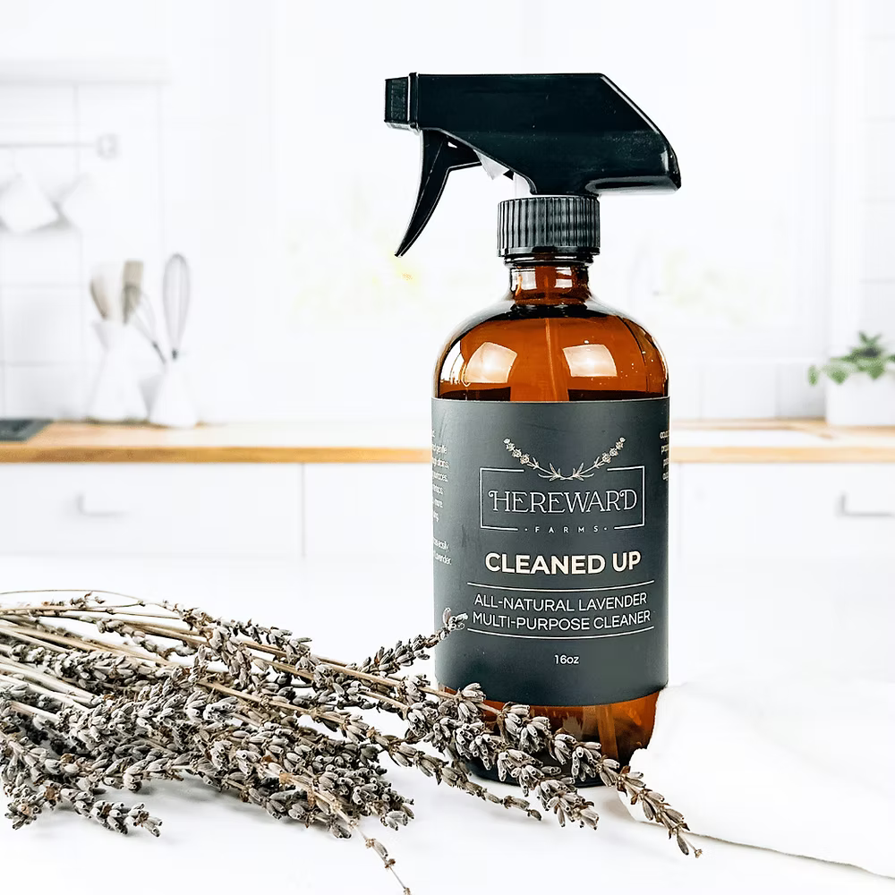 Brown spray bottle labeled 'Cleaned Up' with lavender on a white surface