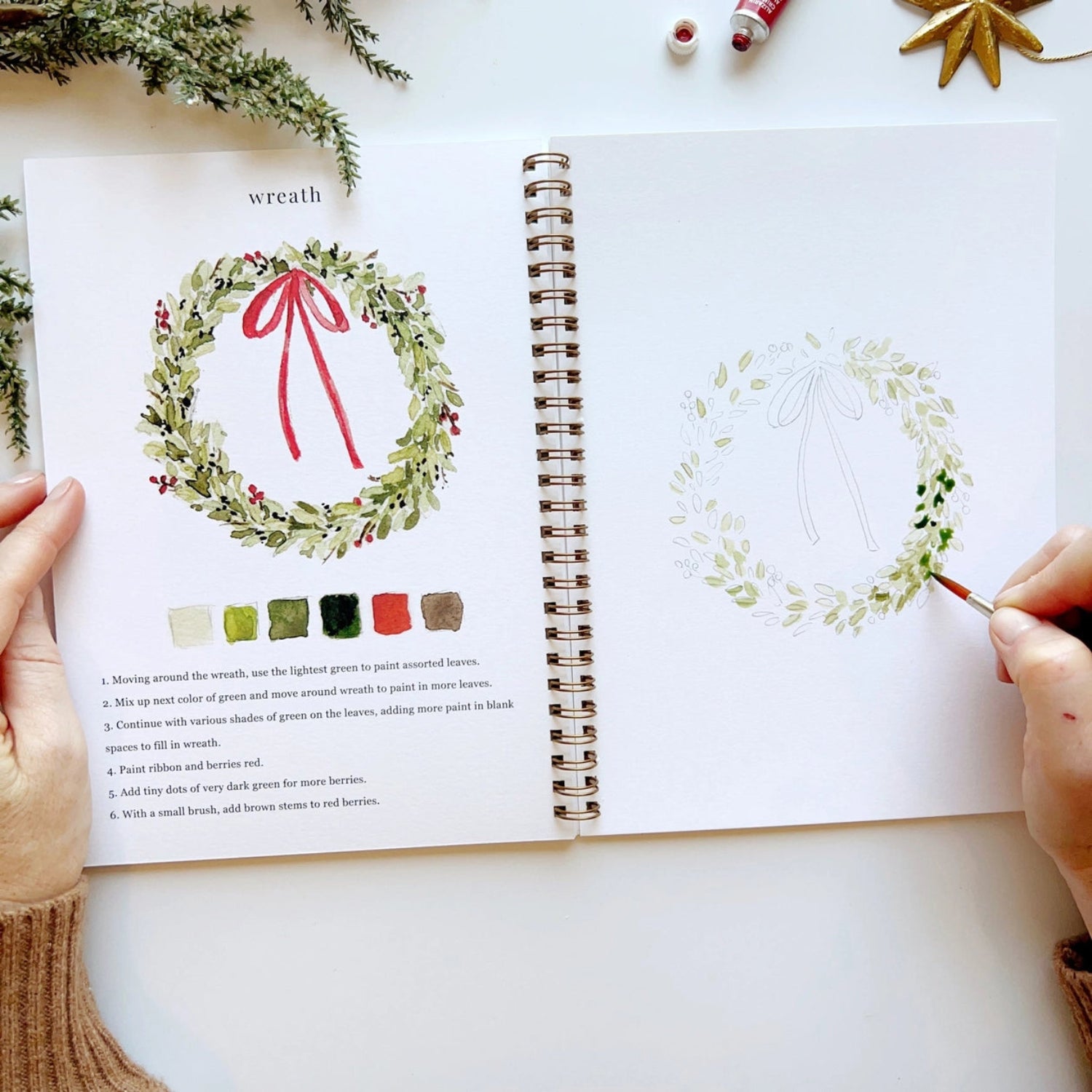 Open book with a wreath illustration and color swatches, being used to create a wreath drawing.