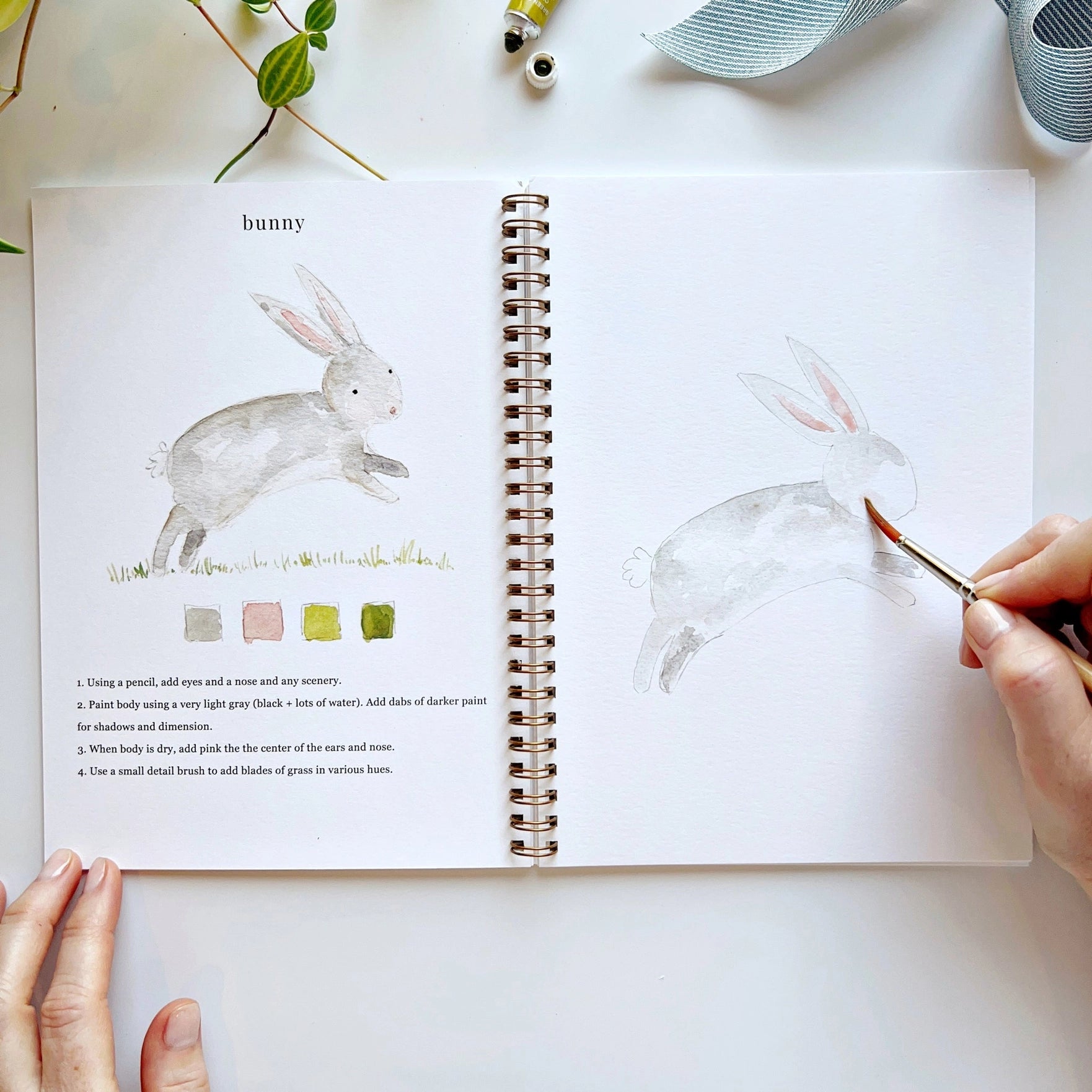 Open book with rabbit illustration and painting activity, hands holding a brush.