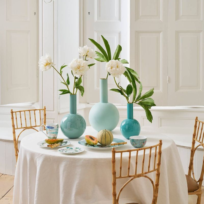 Dining table set with turquoise vases, white flowers, and fruit on a white tablecloth.
