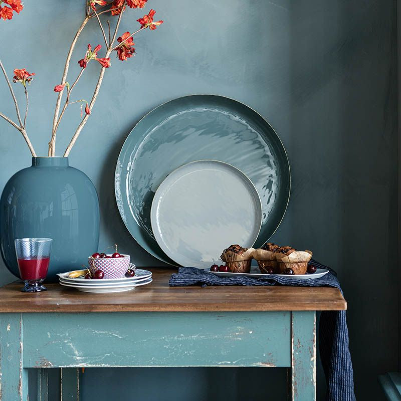 Dining table with plates, glasses, and a pitcher of red liquid against a teal wall.