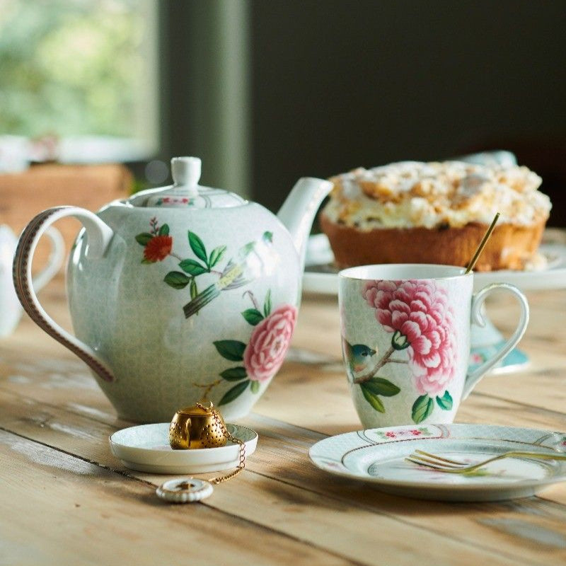 Tea set with floral patterns on a wooden table, blurred greenery in the background